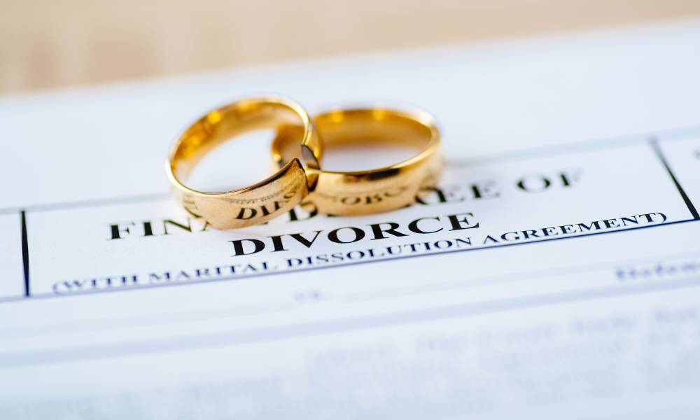 Two golden wedding bands with one partially on top of the other, both placed on paperwork for finalizing divorce.