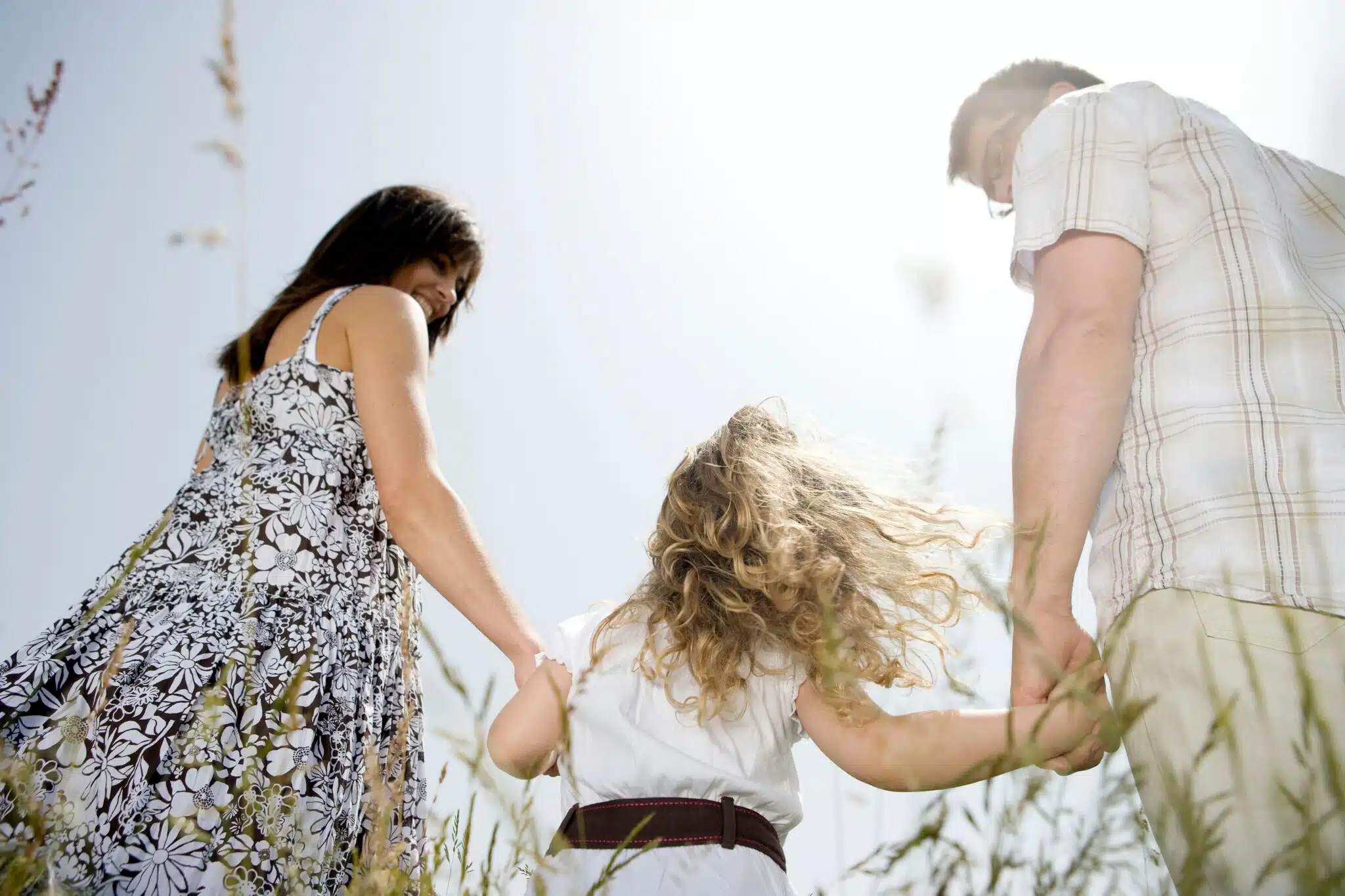 Parents holding child's hands in sunny field