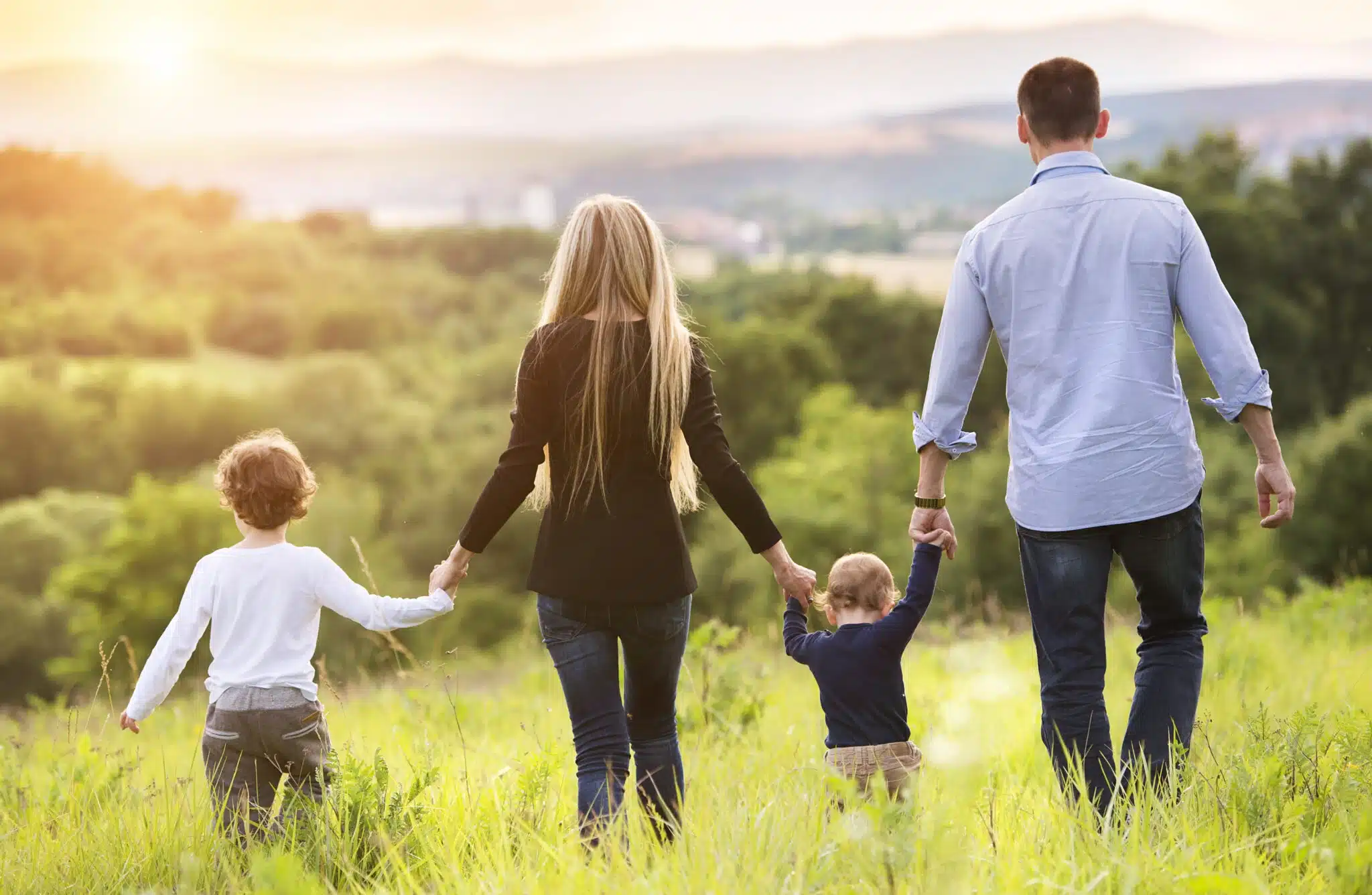 Family of four walking through field at sunset
