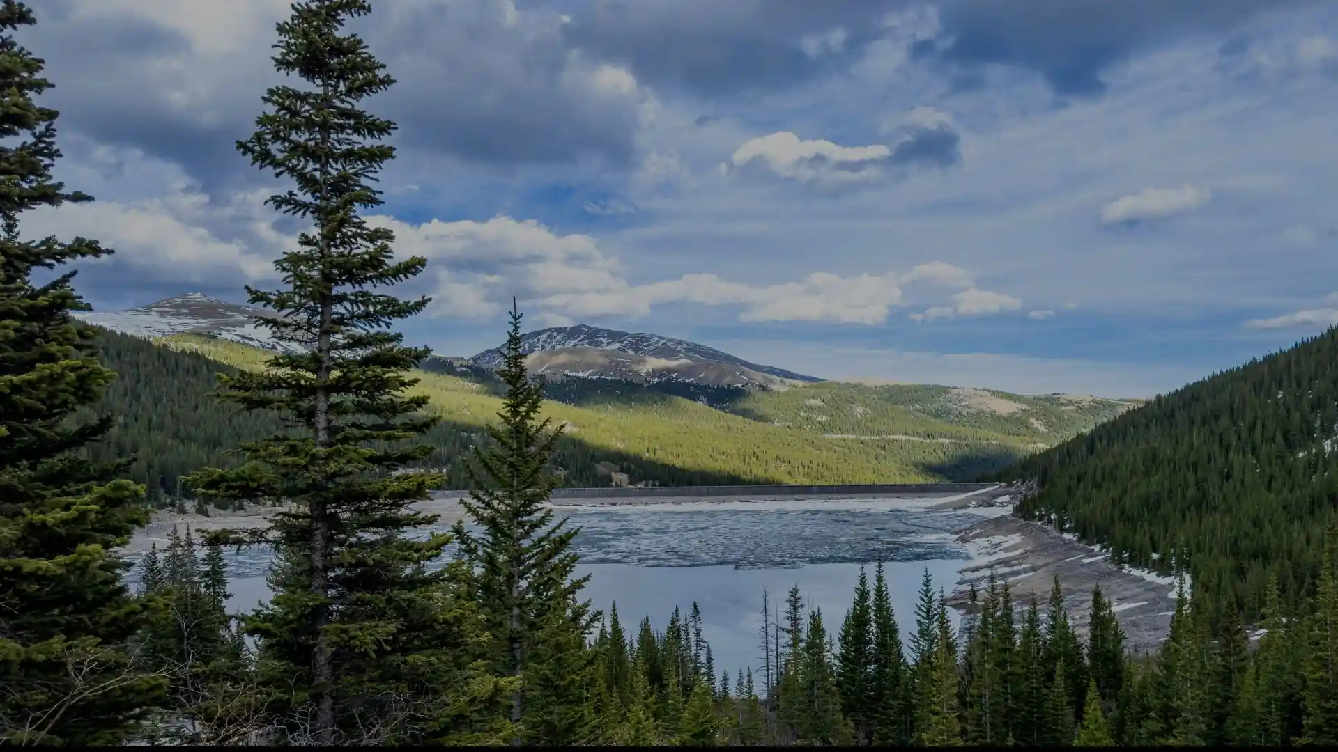 Mountain reservoir surrounded by pine forest and snowcapped peaks