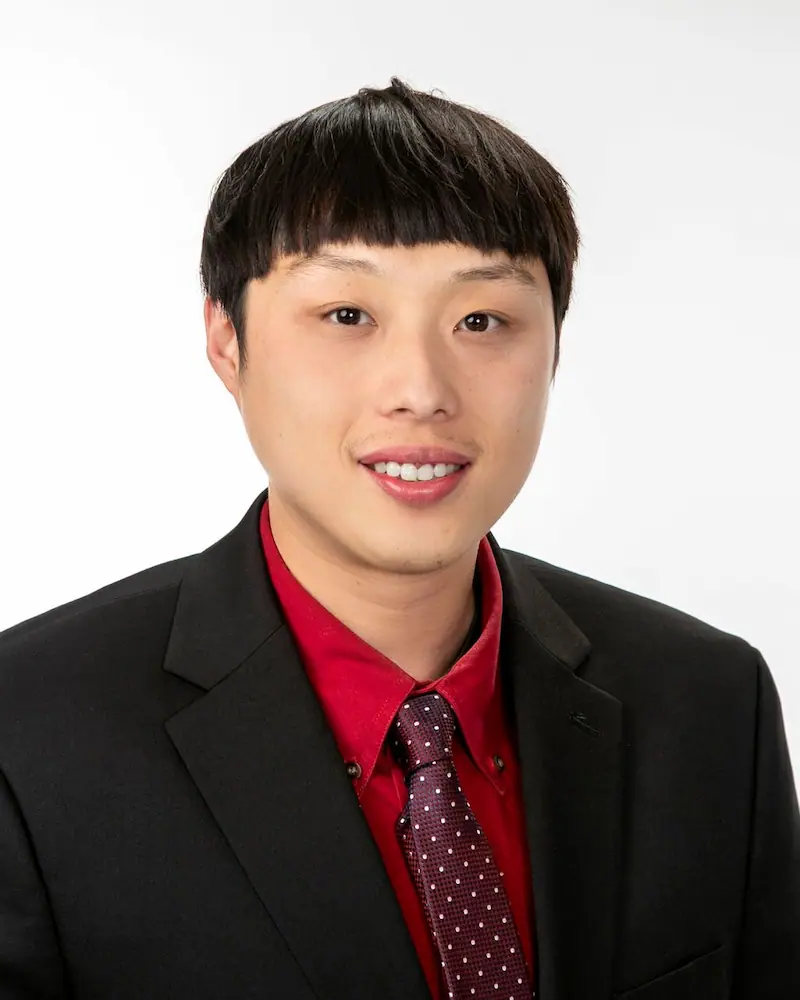 Man in black suit and red shirt smiling