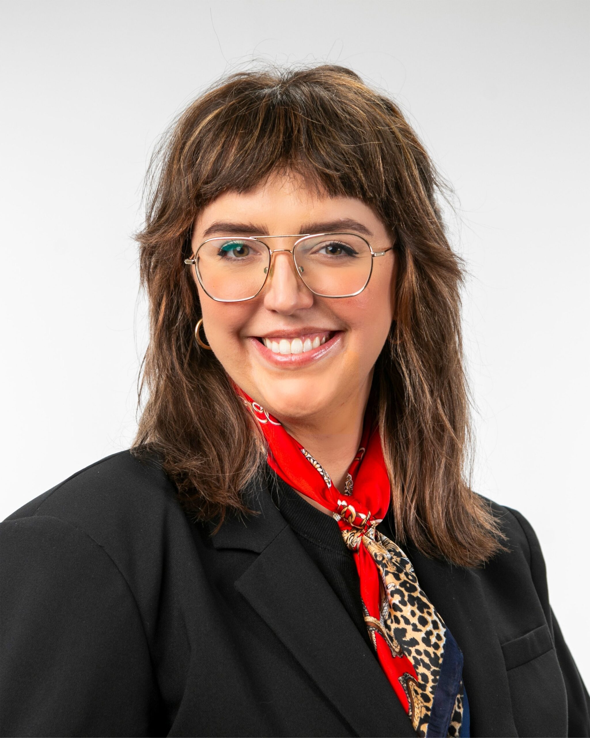Smiling woman in glasses, black blazer, and red scarf