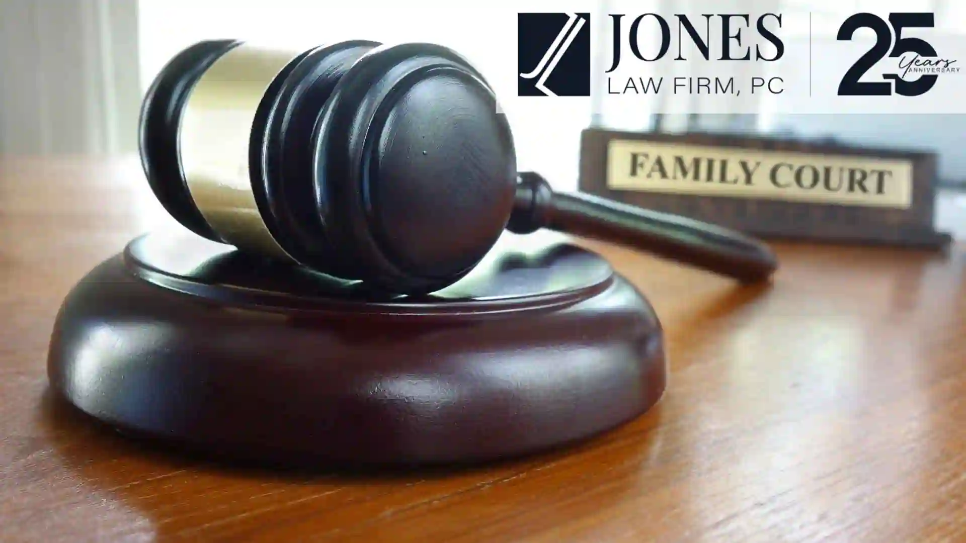 Close-up image of a wooden gavel held by hand on a desk in a courtroom setting, illustrating family lawyer in Centennial. Branded with the Jones Law Firm PC logo.